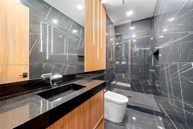 full bathroom with vanity, toilet, a marble finish shower, and tile walls
