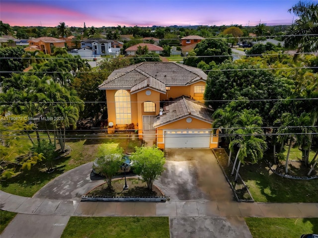view of front of home with a tile roof, a garage, concrete driveway, stucco siding, and fence