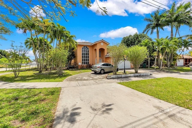 mediterranean / spanish home with stucco siding, a tiled roof, a front lawn, and curved driveway