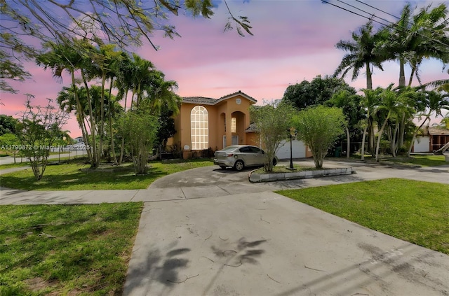 mediterranean / spanish-style house with a tile roof, a yard, stucco siding, and curved driveway