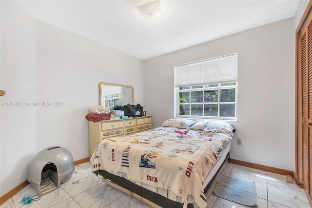 bedroom featuring marble finish floor, a closet, a textured ceiling, and baseboards