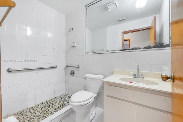 bathroom featuring tile walls, tiled shower, vanity, tile patterned floors, and toilet