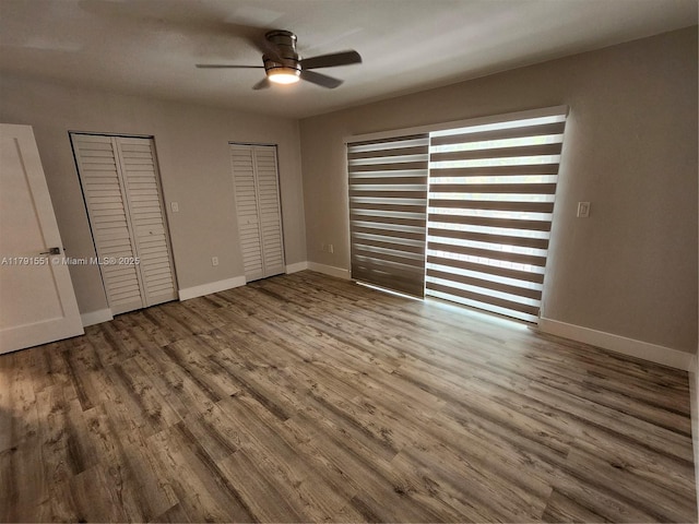 unfurnished bedroom with a ceiling fan, wood finished floors, multiple closets, and baseboards
