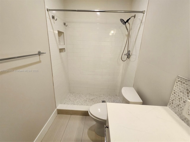 full bathroom with baseboards, a tile shower, toilet, and vanity