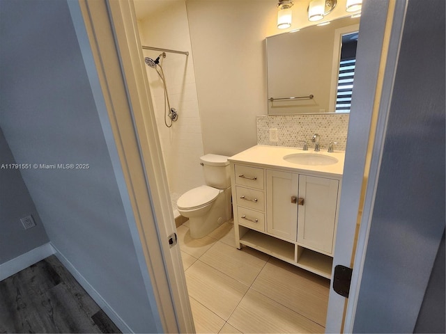 bathroom with toilet, vanity, decorative backsplash, and tiled shower