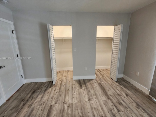 unfurnished bedroom featuring a closet, baseboards, wood finished floors, and a spacious closet