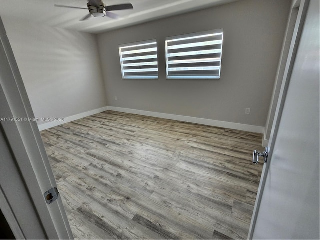 spare room with wood finished floors, a ceiling fan, and baseboards