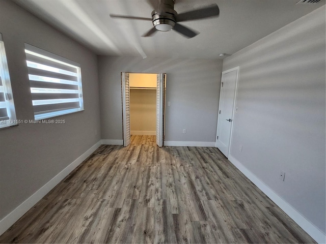 unfurnished bedroom featuring a walk in closet, wood finished floors, and baseboards
