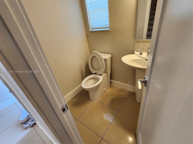 bathroom with toilet, baseboards, tile patterned flooring, and a sink