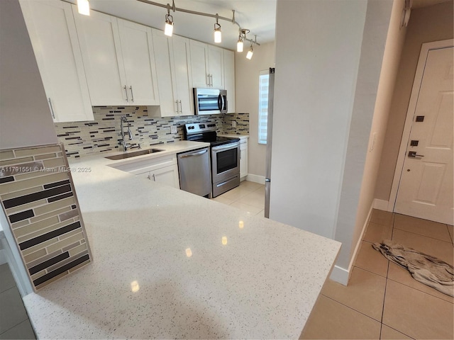 kitchen featuring light stone countertops, a sink, backsplash, white cabinets, and appliances with stainless steel finishes