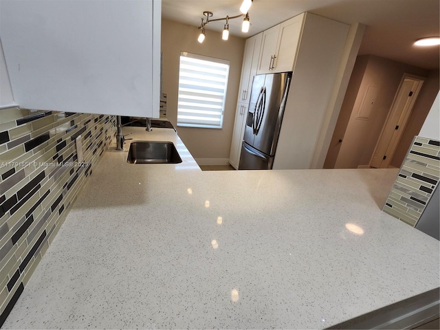 kitchen featuring light stone countertops, stainless steel refrigerator with ice dispenser, decorative backsplash, and a sink