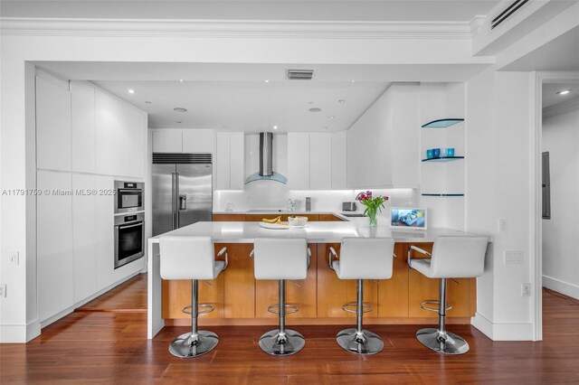 kitchen with modern cabinets, stainless steel appliances, visible vents, a peninsula, and wall chimney range hood