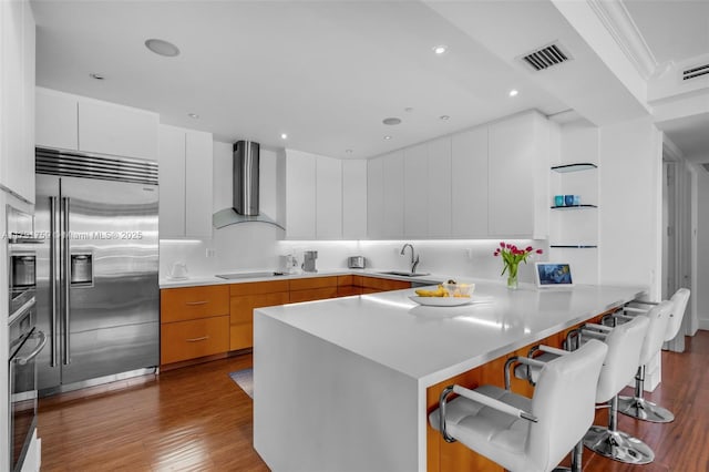 kitchen featuring a peninsula, stainless steel appliances, a sink, visible vents, and wall chimney exhaust hood