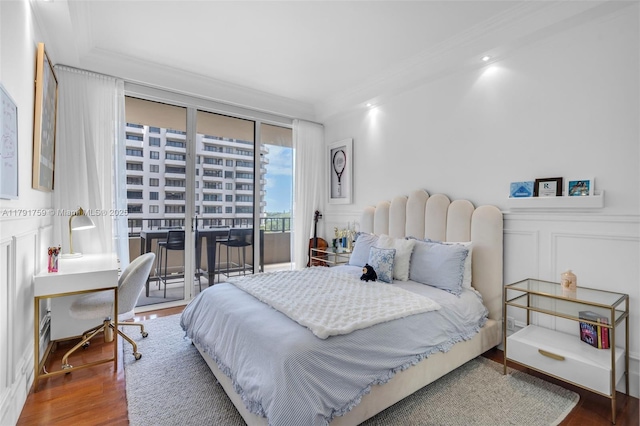 bedroom with wood finished floors, access to exterior, crown molding, and a decorative wall