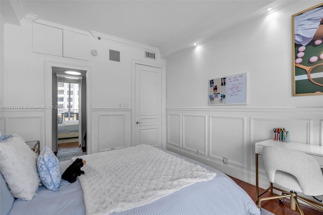 bedroom featuring ornamental molding, visible vents, wood finished floors, and a decorative wall