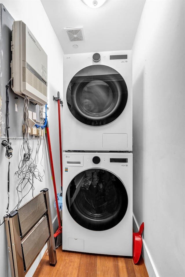 washroom featuring wood finished floors, visible vents, stacked washer / dryer, and laundry area