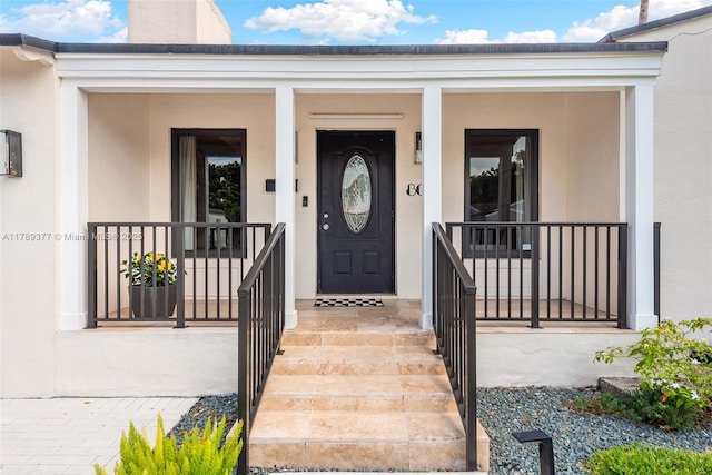 view of exterior entry with stucco siding and a porch