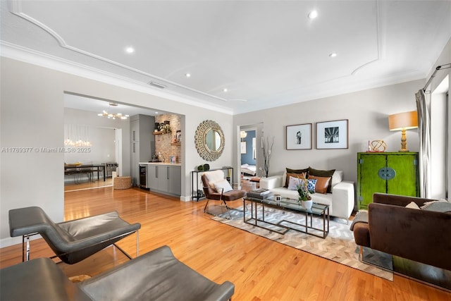 living area featuring crown molding, visible vents, an inviting chandelier, light wood-type flooring, and recessed lighting