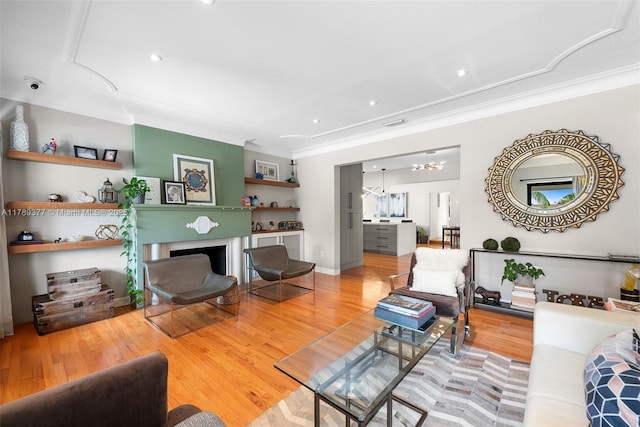 living area featuring ornamental molding, a notable chandelier, wood finished floors, and a fireplace