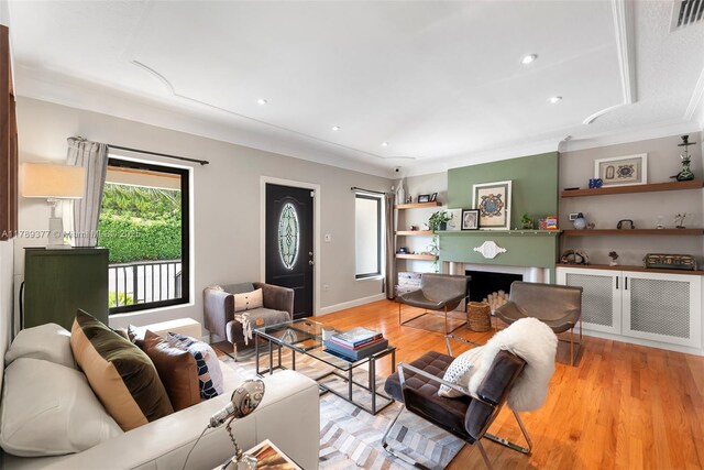 living area with crown molding, visible vents, light wood-type flooring, recessed lighting, and a fireplace