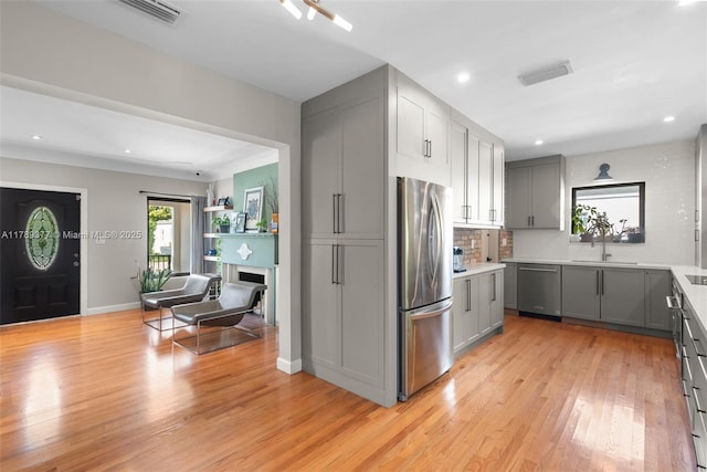 kitchen with a sink, gray cabinets, light wood-style flooring, and stainless steel appliances