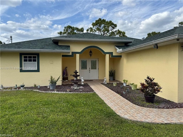 1127 Foggia St E, Lehigh Acres, FL 33974 - view of exterior entry featuring roof with shingles, stucco siding, and a lawn