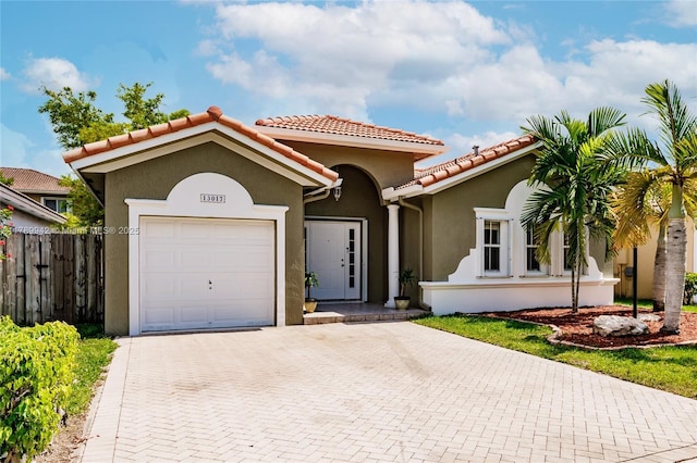 mediterranean / spanish-style home with stucco siding, a tiled roof, fence, decorative driveway, and a garage