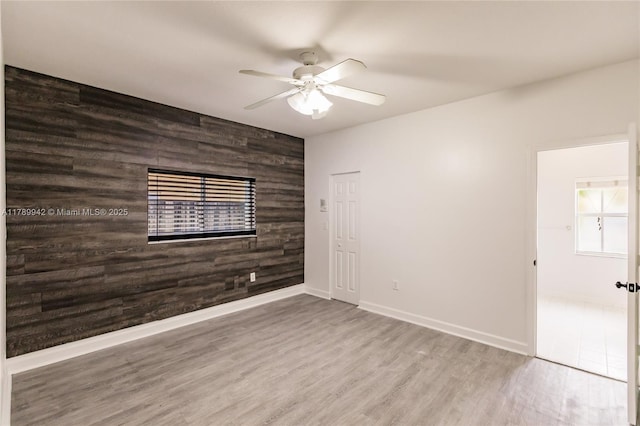 spare room featuring ceiling fan, wood walls, baseboards, an accent wall, and wood finished floors