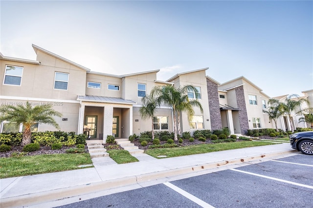 townhome / multi-family property with a standing seam roof, stucco siding, uncovered parking, and metal roof