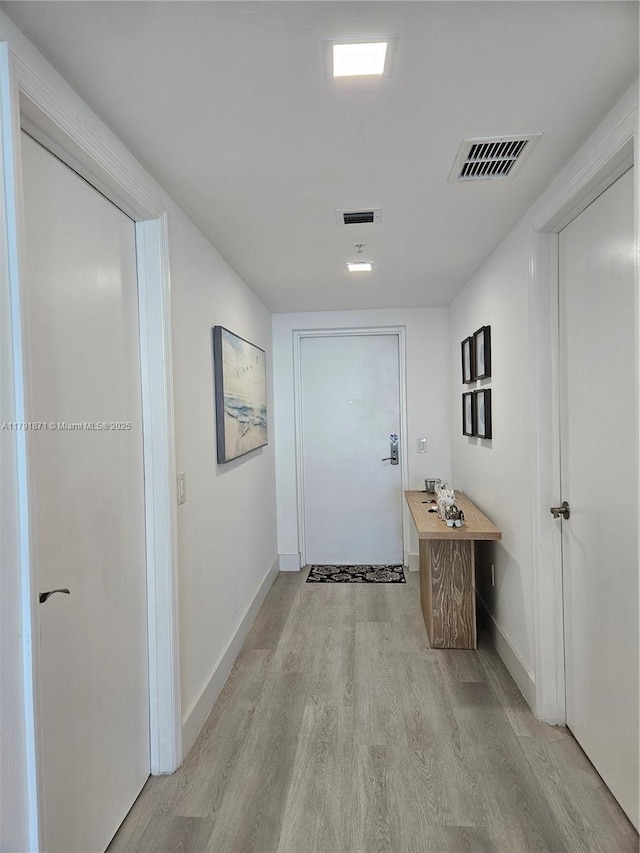 hallway with visible vents, light wood-style floors, and baseboards