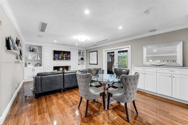 dining area with a textured ceiling, crown molding, light wood-style flooring, visible vents, and a fireplace