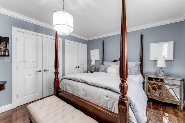 bedroom featuring crown molding, a notable chandelier, two closets, and wood finished floors