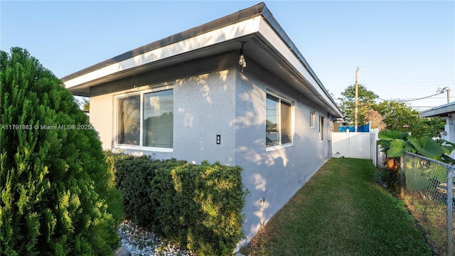 view of property exterior with a yard, stucco siding, and fence
