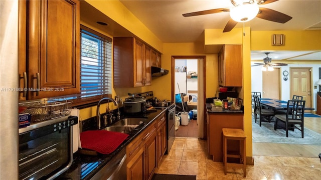 kitchen featuring appliances with stainless steel finishes, brown cabinets, dark countertops, ceiling fan, and a sink