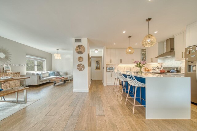 kitchen featuring visible vents, a kitchen bar, wall chimney exhaust hood, white cabinetry, and stainless steel appliances