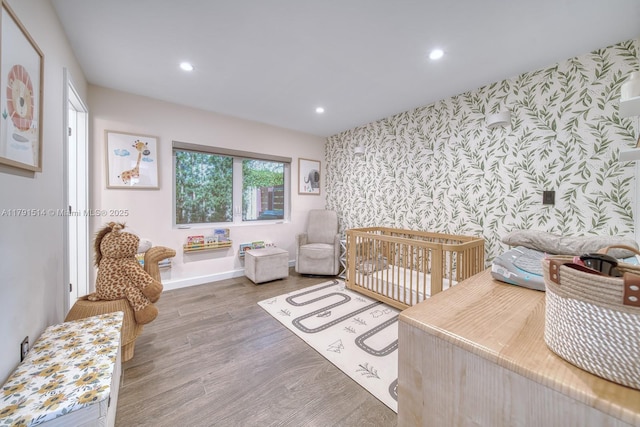 bedroom with wood finished floors, baseboards, wallpapered walls, an accent wall, and recessed lighting
