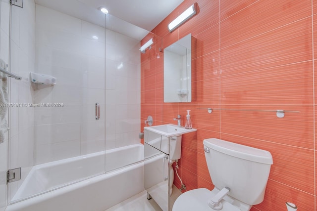 bathroom with tile walls, toilet, and shower / bath combination with glass door