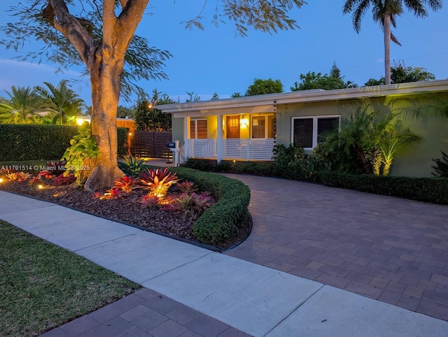 ranch-style home featuring a porch, stucco siding, and fence