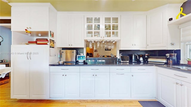 kitchen with light wood-style floors, a sink, white cabinetry, and glass insert cabinets