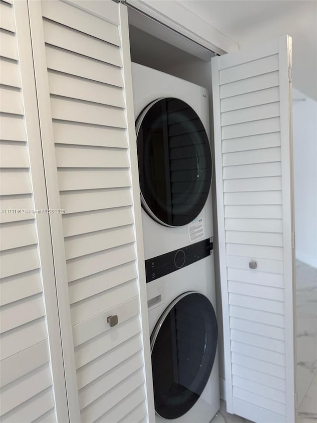 clothes washing area featuring stacked washer and clothes dryer, laundry area, and marble finish floor