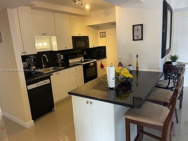 4400 Hillcrest Dr Unit 701B, Hollywood, FL 33021 - kitchen with white cabinets, dark countertops, a breakfast bar, a sink, and black appliances