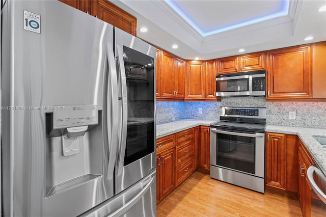 300 SW 130th Ter Unit 203B, Pembroke Pines, FL 33027 - kitchen featuring appliances with stainless steel finishes, a tray ceiling, brown cabinets, light wood-type flooring, and light stone countertops