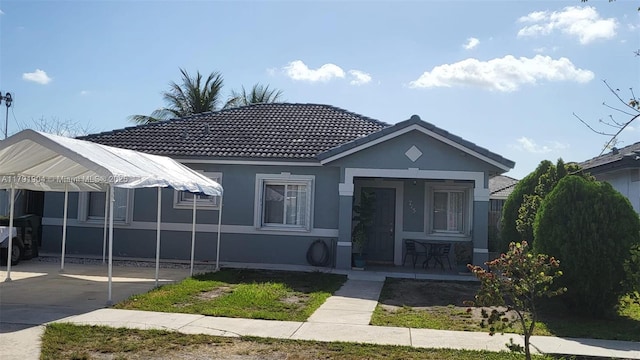 bungalow featuring a porch, stucco siding, a tiled roof, and a carport