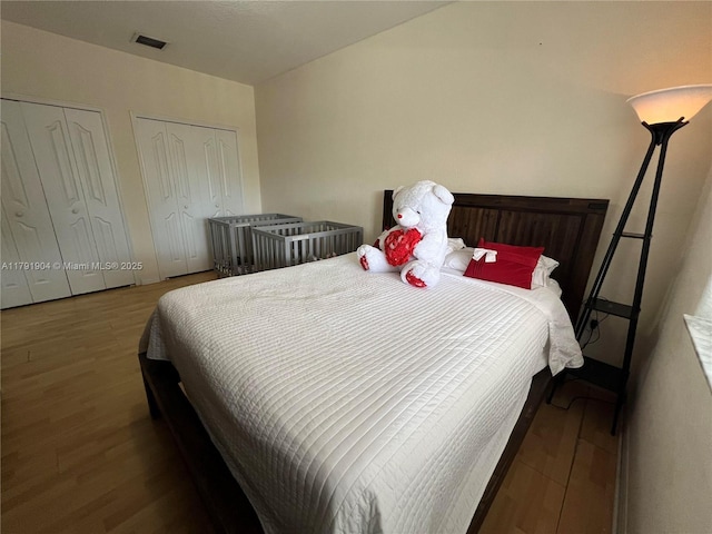 bedroom featuring two closets, visible vents, and wood finished floors