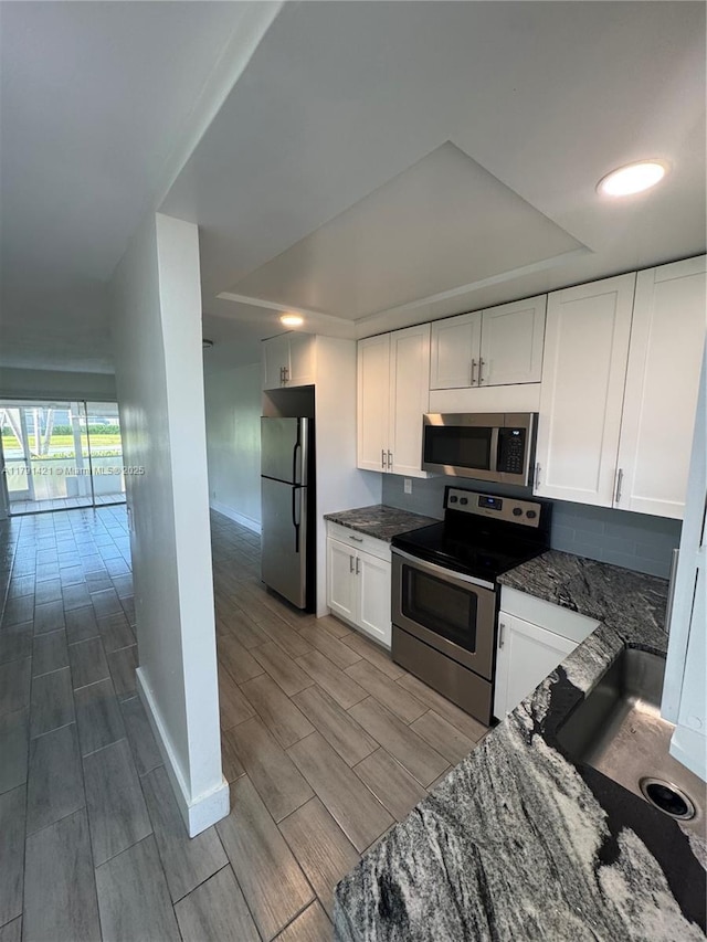 9851 Sandalfoot Blvd Unit 208, Boca Raton, FL 33428 - kitchen featuring appliances with stainless steel finishes, a raised ceiling, wood finish floors, dark stone countertops, and white cabinetry