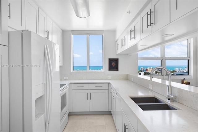 kitchen featuring a sink, light stone countertops, white appliances, and a healthy amount of sunlight