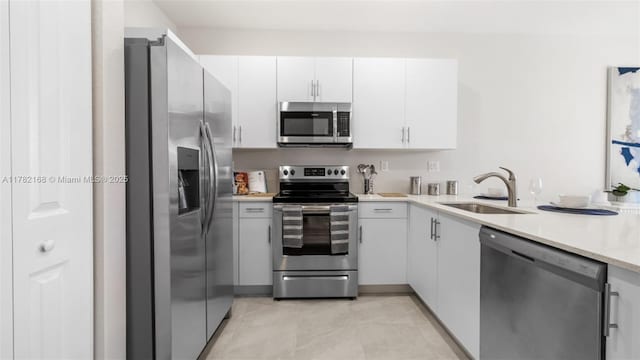 kitchen with appliances with stainless steel finishes, light countertops, a sink, white cabinetry, and light tile patterned flooring