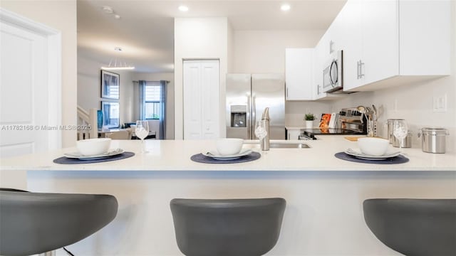 kitchen featuring a breakfast bar, stainless steel appliances, a sink, white cabinetry, and a peninsula