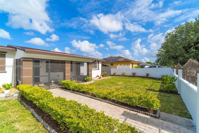 back of house with a fenced backyard, stucco siding, a sunroom, and a lawn