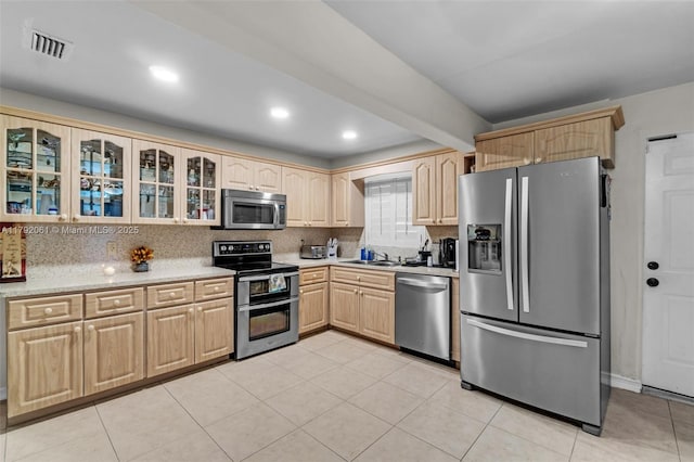 kitchen with glass insert cabinets, light brown cabinets, appliances with stainless steel finishes, a sink, and visible vents
